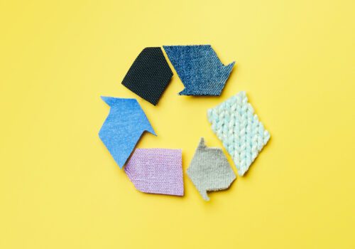 Reuse, reduce, recycle concept background. Recycle symbol made from old clothing on yellow background. Top view or flat lay.